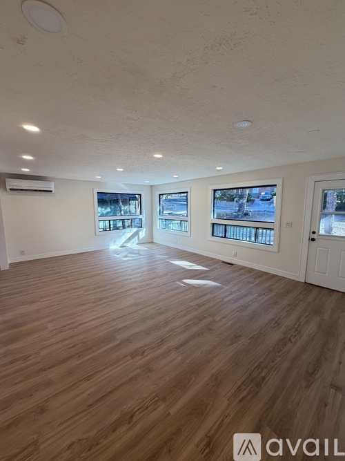 A spacious room with wooden flooring and a large window overlooking a snowy landscape.