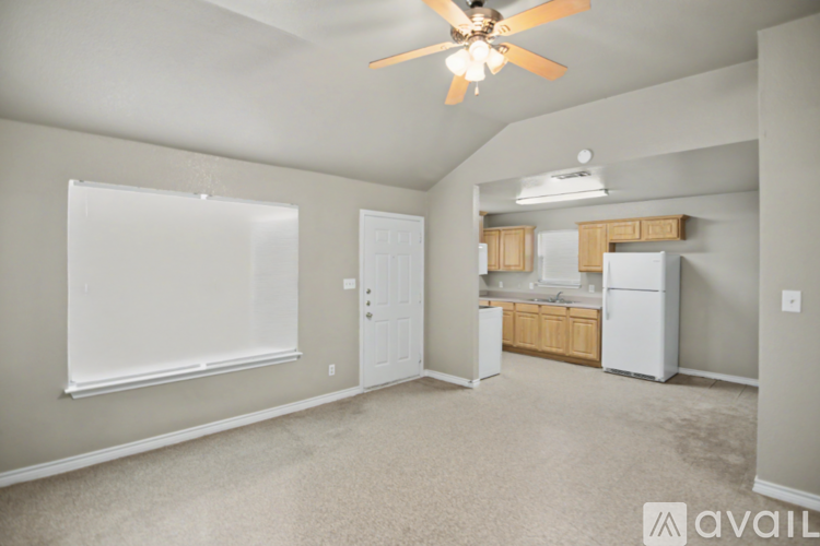 A living room with a ceiling fan and a kitchen area in the background.