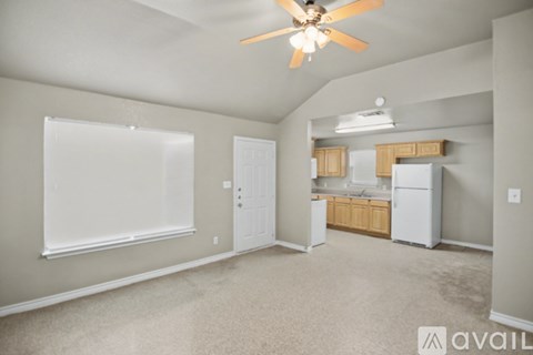 A living room with a ceiling fan and a kitchen area in the background.