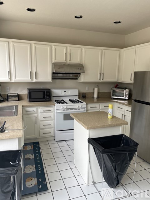 A kitchen with white cabinets and a black trash bag in the trash can.