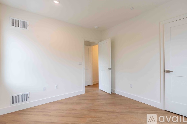 A spacious room with wooden floors and white walls, with a doorway leading to another room.