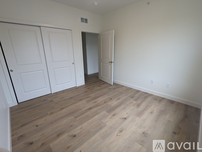 A room with wooden flooring and white walls, featuring a white door and two white closet doors.