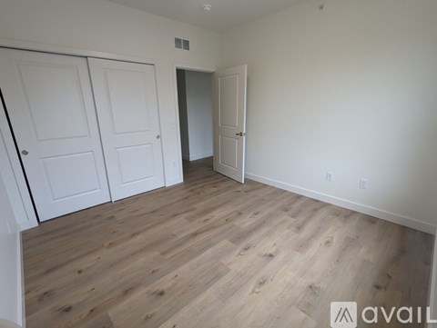 A room with wooden flooring and white walls, featuring a white door and two white closet doors.