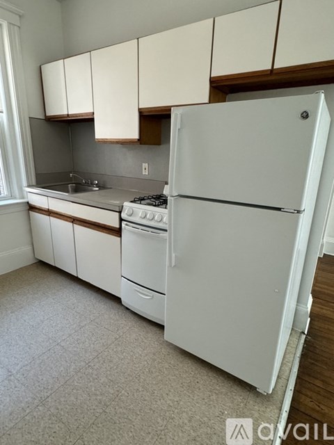 A white refrigerator stands in a kitchen with white cabinets.