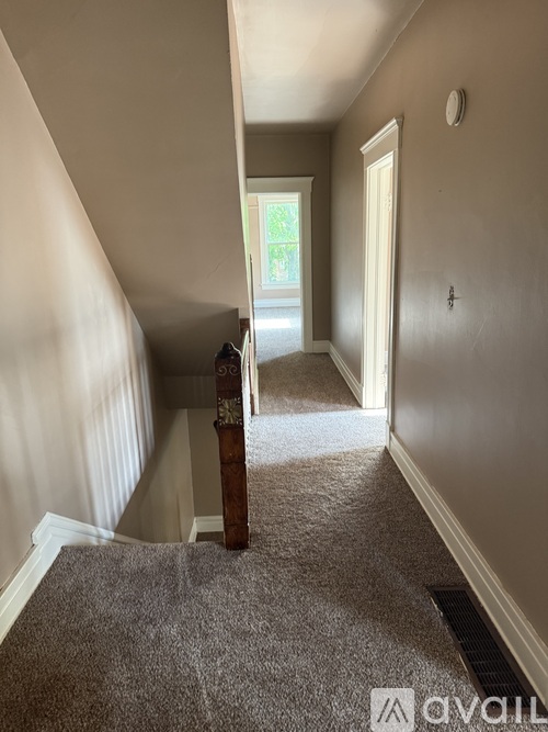 A hallway with a carpeted floor and a wooden staircase.