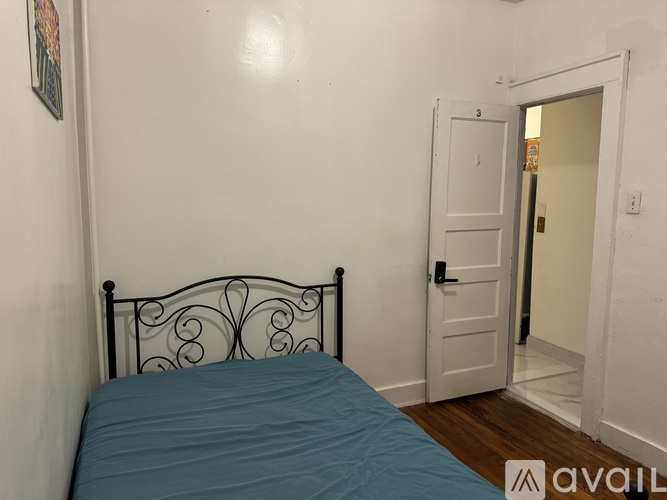 A bed with a blue cover sits in a room with a door and a wall hanging.