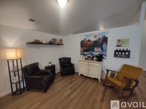 A living room with a wooden floor and white walls, furnished with a black leather chair, a wooden chair, and a wooden cabinet.