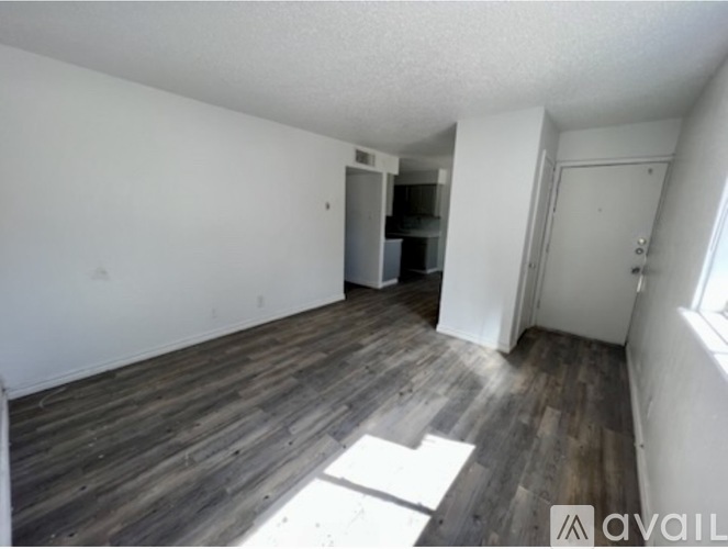 A room with wooden floors and white walls, with a door on the right and a small closet with a door on the left.