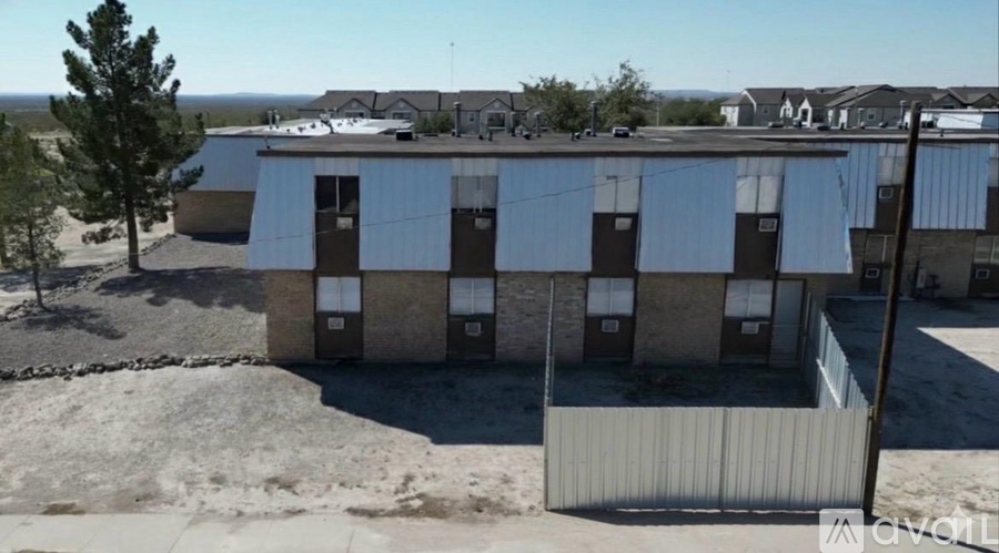 A building with a brown facade and a grey roof is surrounded by a fence.
