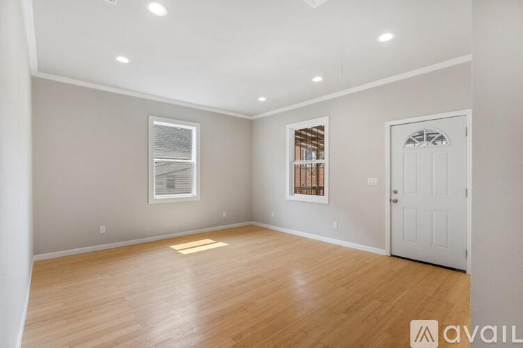 A room with wooden floors and white walls, with a window and a door.