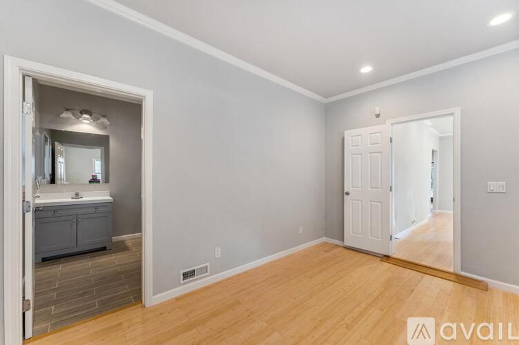 A room with wooden floors and a bathroom visible through the open door.