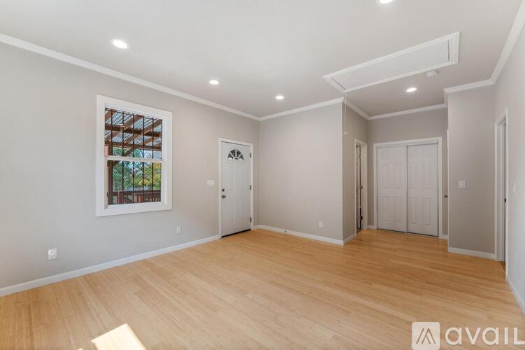 A spacious room with wooden flooring and white walls.