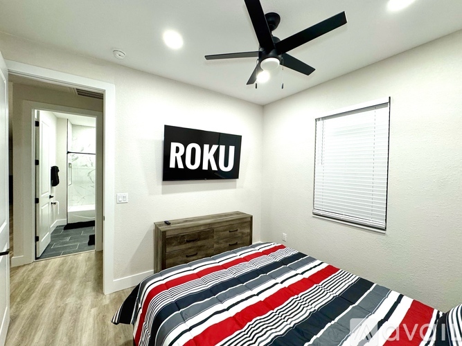 A bedroom with a bed, a dresser, and a ROKU sign on the wall.