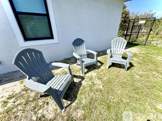 Three Adirondack chairs are placed on the grass outside a house.