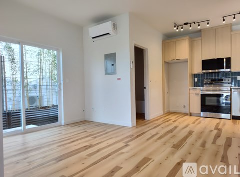A spacious room with wooden flooring and a kitchen area with stainless steel appliances.