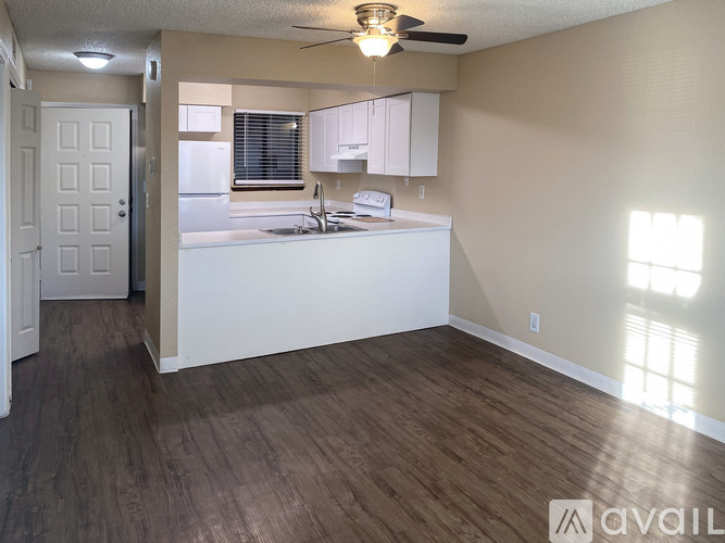 A well-lit kitchen and living room with a ceiling fan and wooden flooring.