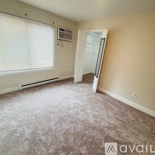 A carpeted room with a window and a door leading to another room.