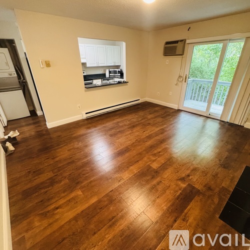 A room with wooden flooring and a window overlooking a kitchen.