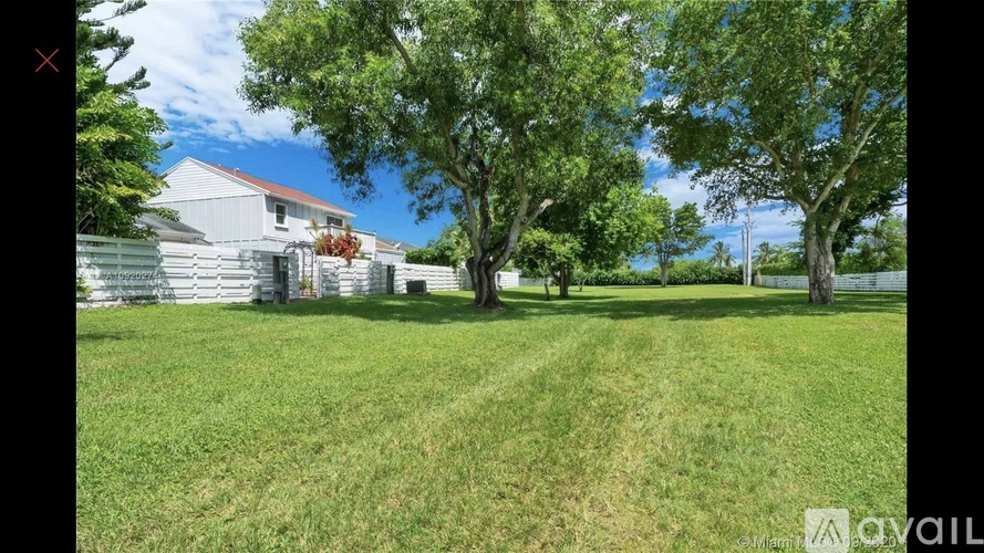 A white house with a red roof is surrounded by a grassy yard and trees.