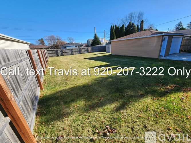 A house with a brown siding and a white door is surrounded by a grassy lawn.