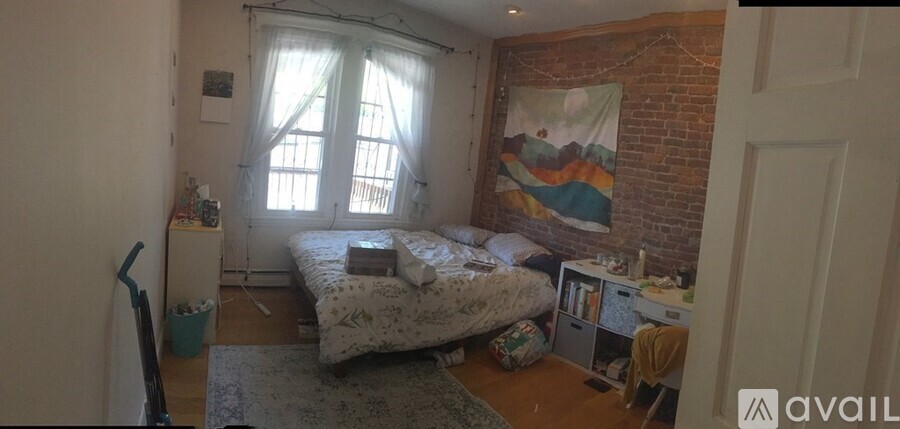 A bedroom with a bed, a desk, and a window with white curtains.