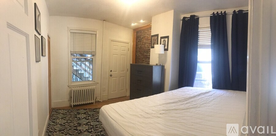 A bedroom with a large bed and a window with black curtains.