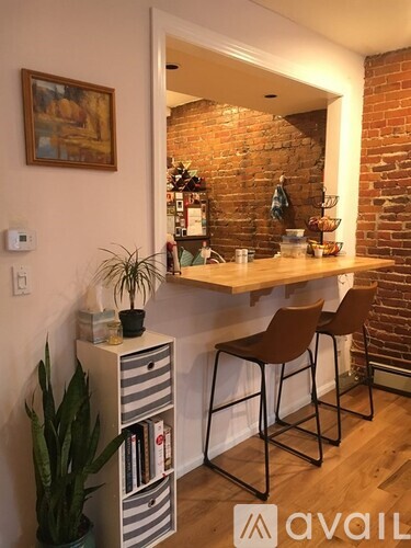 A room with a brick wall and a white shelf with two chairs.