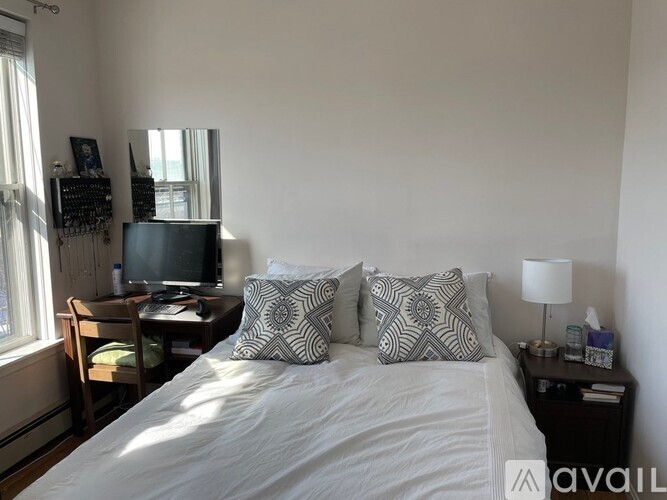 A bedroom with a bed, a desk with a computer, and a window with curtains.