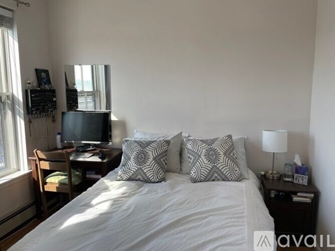 A bedroom with a bed, a desk with a computer, and a window with curtains.
