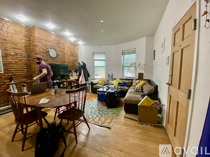 A man is working on his laptop in a room with a brick wall.