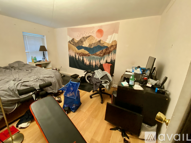 A room with a mountain painting on the wall and a bed with a grey blanket.