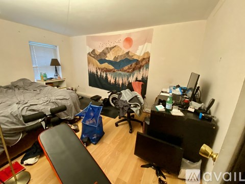 A room with a mountain painting on the wall and a bed with a grey blanket.