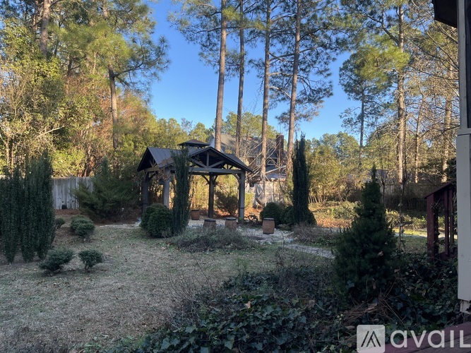 A gazebo is surrounded by trees and bushes in a yard.