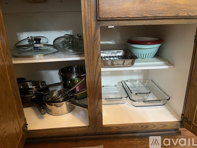 A kitchen cabinet with a glass door is open, revealing a variety of cookware.