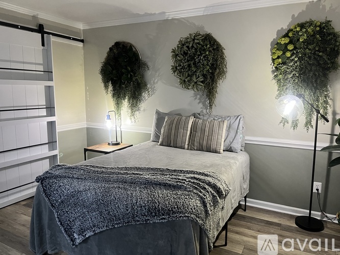 A bedroom with a bed covered in a grey blanket and two hanging green plants.