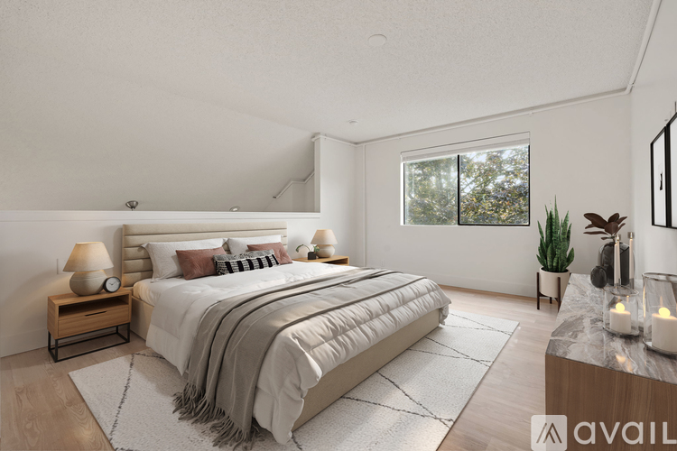 A well-lit bedroom with a large bed and a window showing greenery outside.