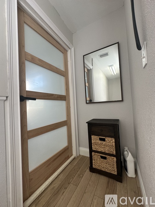 A hallway with a wooden door, a mirror, and a wooden cabinet with baskets.