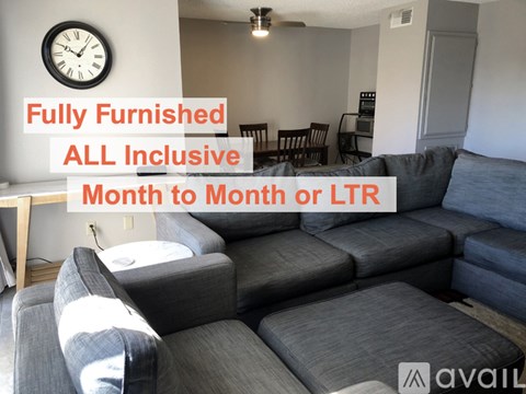 A fully furnished living room with a grey sofa and a clock on the wall.