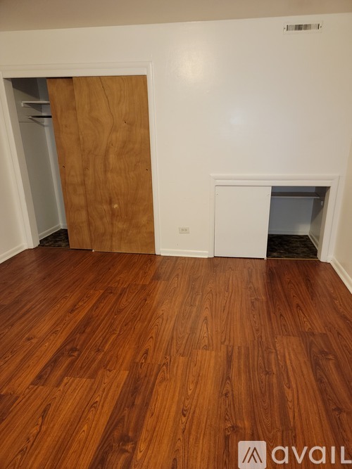 A room with wooden flooring and a white wall with a door.