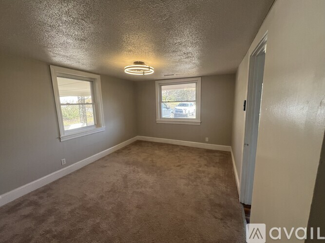 A room with carpeted floor, two windows, and a door.