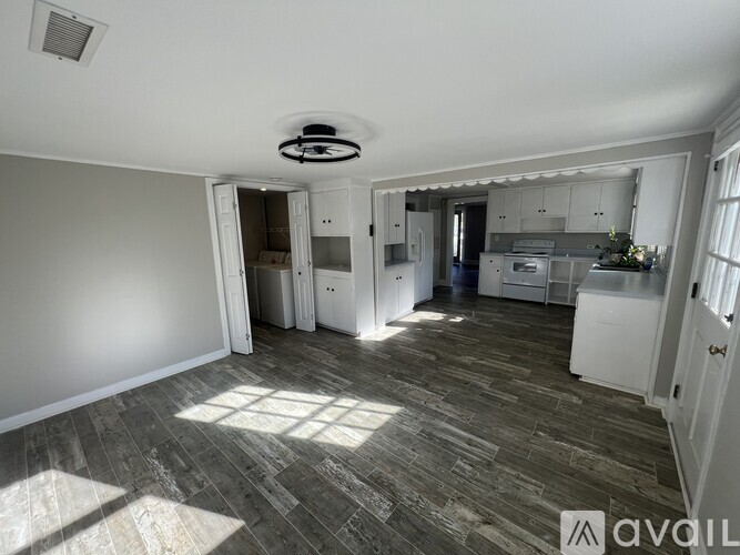 A room with a ceiling fan and a kitchen area in the background.