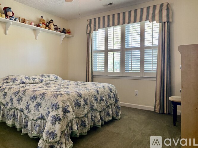 A bedroom with a bed, a window with striped curtains, and a shelf with figurines.