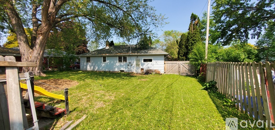 A backyard with a white house, green grass, and a wooden fence.