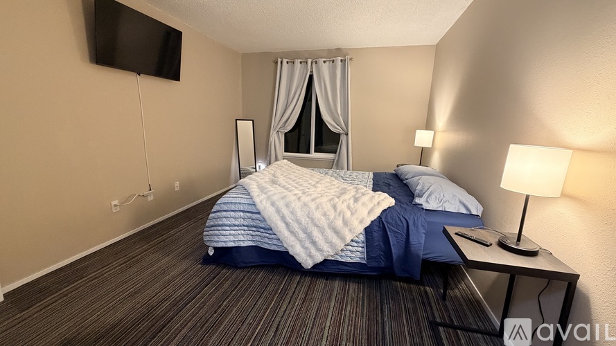 A bedroom with a bed, a nightstand with a lamp, and a flat-screen TV mounted on the wall.