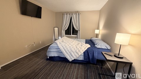 A bedroom with a bed, a nightstand with a lamp, and a flat-screen TV mounted on the wall.