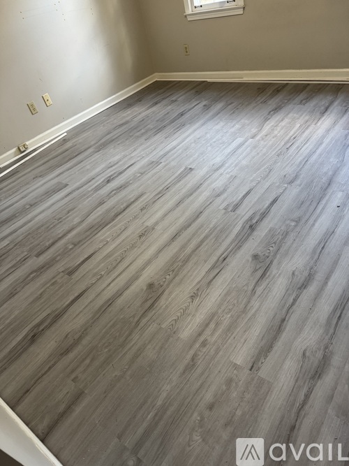 A room with a grey wooden floor and a window.