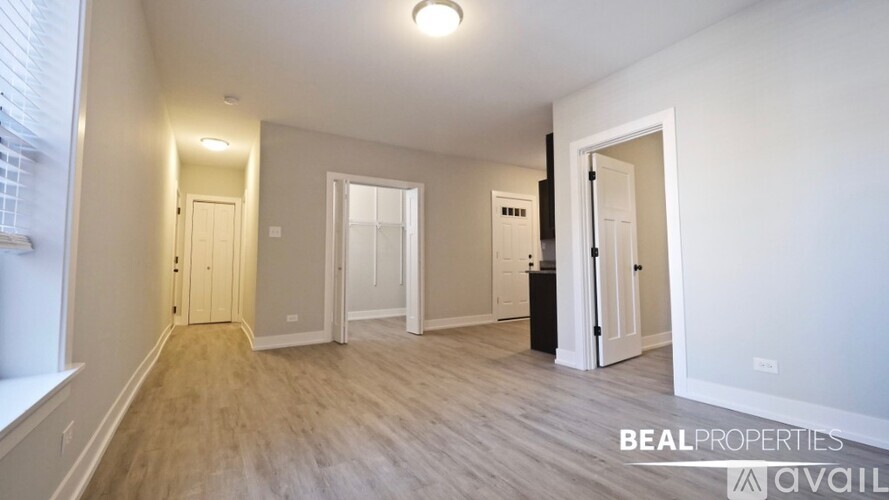A spacious room with wooden flooring and white walls, with a window on the left side.