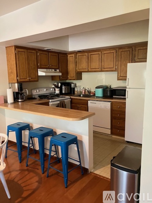 A kitchen with a white fridge, wooden cabinets, and blue stools.