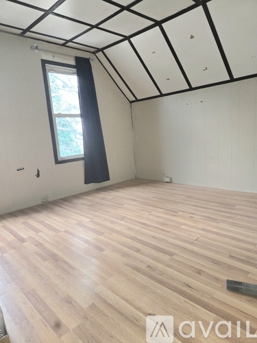 A room with wooden flooring and a window with a black frame.