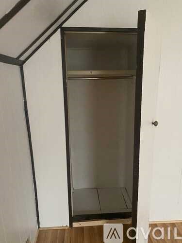 A tall, empty, black and white cabinet with a glass door stands in a room.